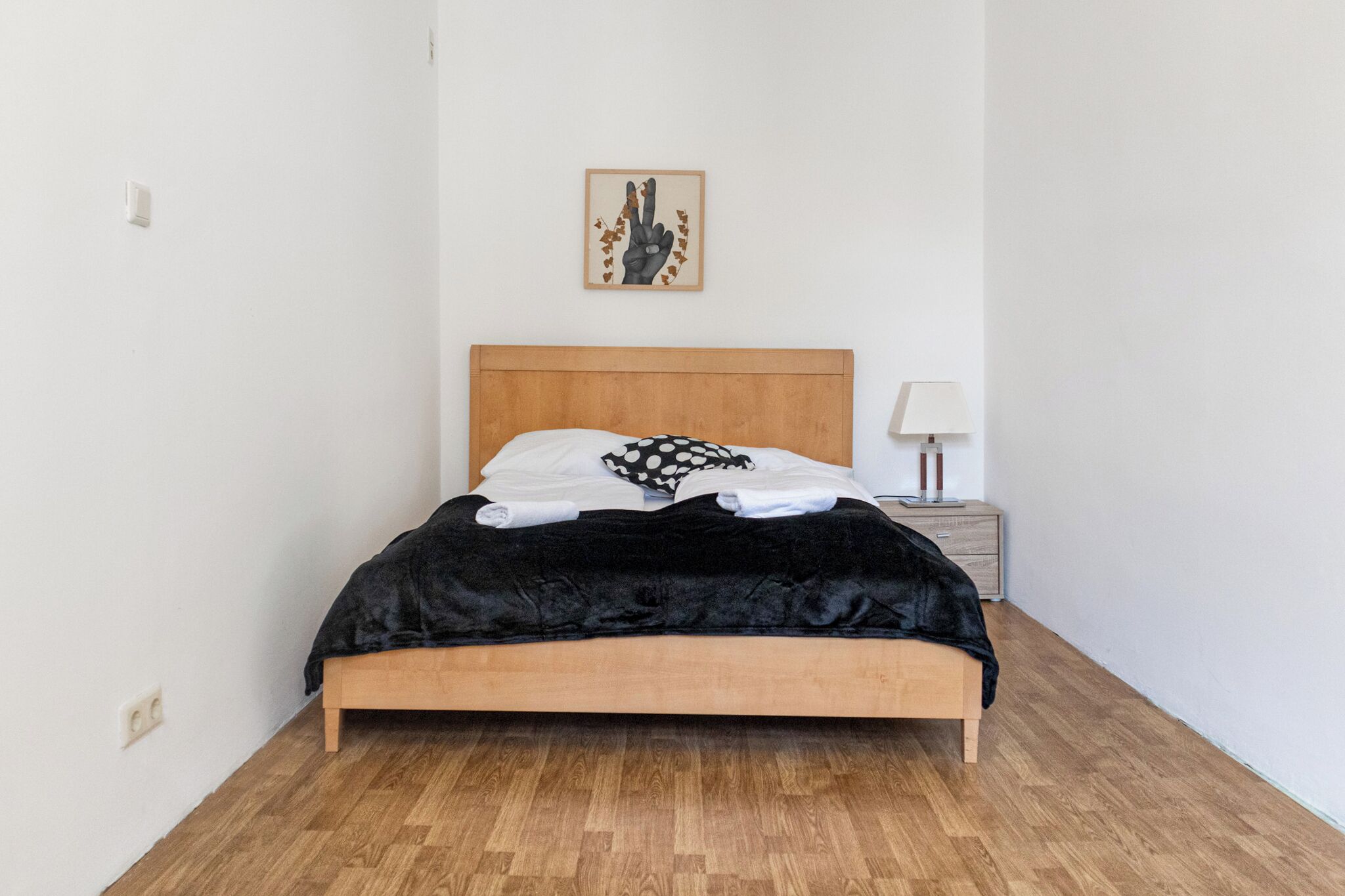Een net opgemaakt bed met een zwart-wit stippenkussen, een houten hoofdbord en een klein nachtkastje met een lamp.