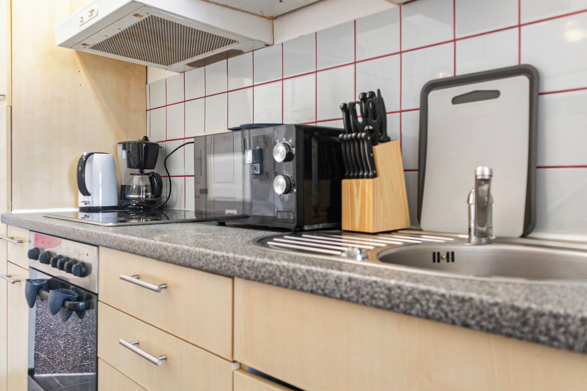 A kitchen with a microwave, toaster, coffee maker, sink, and a knife block.