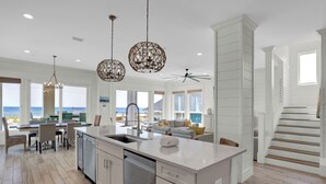 Een ruime keuken met een groot eiland, moderne hanglampen en uitzicht op zee.
