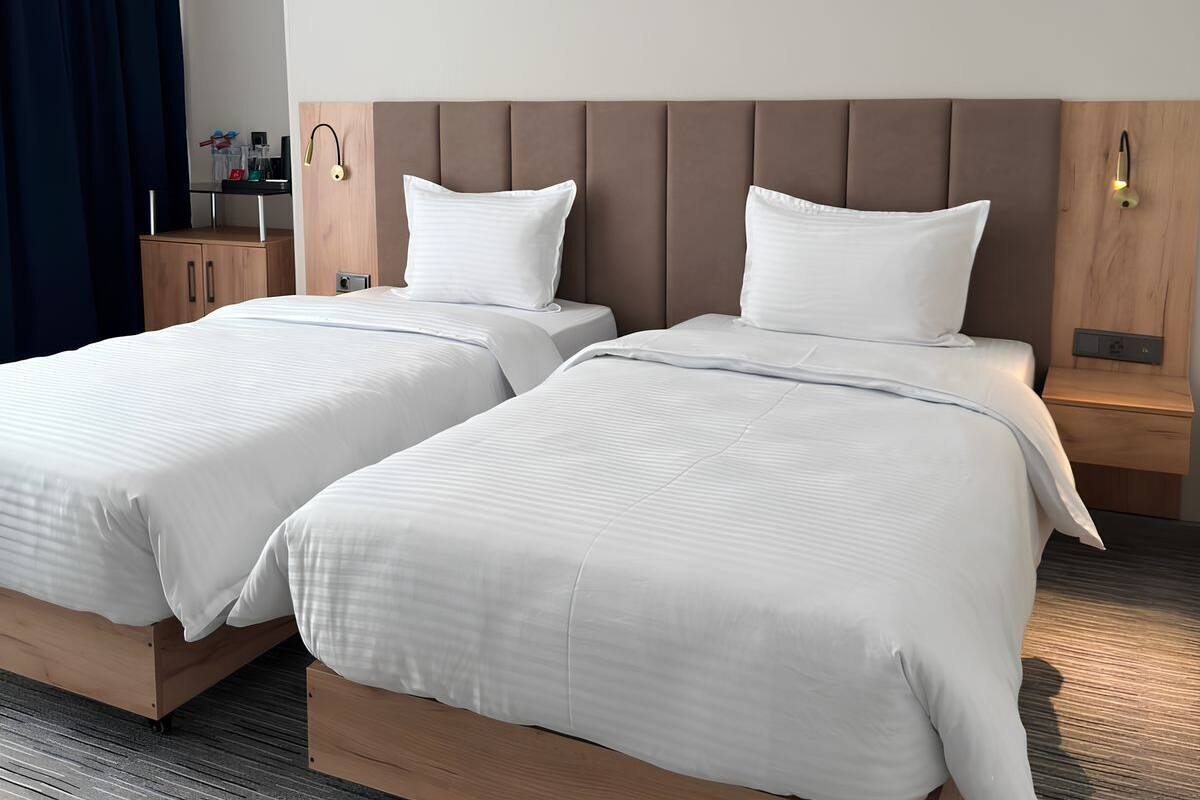 A hotel room with two beds, a wooden headboard, bedside tables, and a small desk with a lamp.