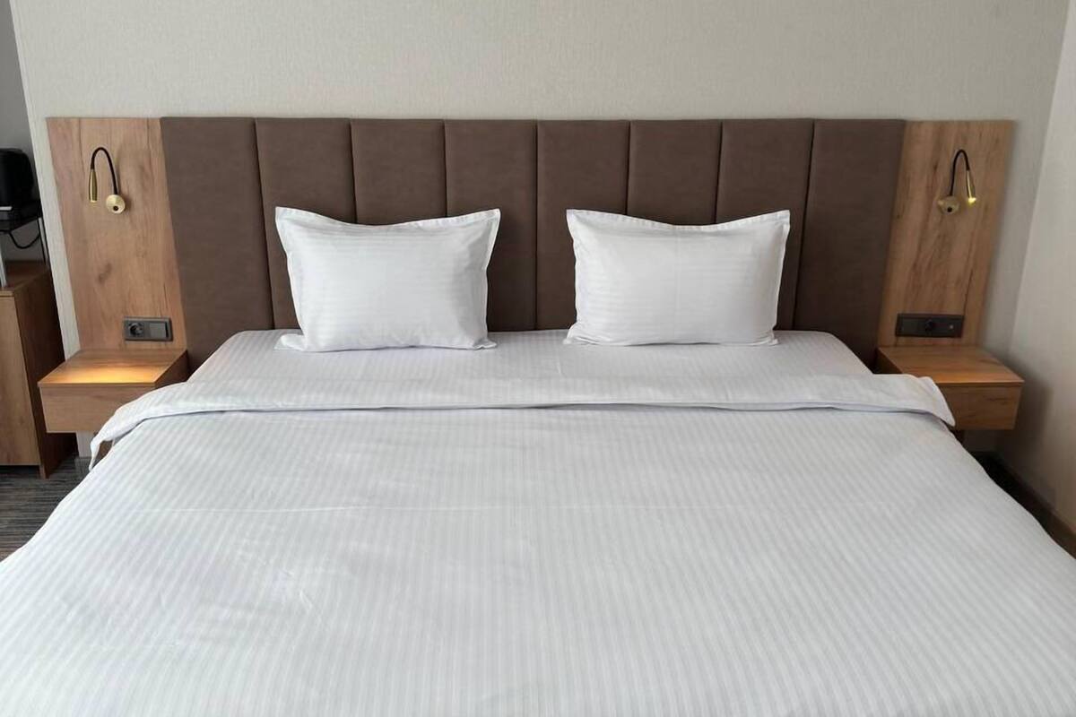A double bed with a wooden headboard, two white pillows, and bedside tables with lamps.