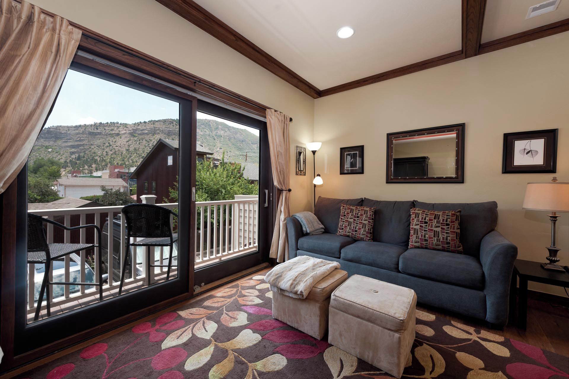 A living room with a sofa, ottoman, and a view of a mountain landscape through a sliding glass door.