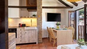 Una cucina moderna con un pilastro in pietra, travi in legno a soffitto e zona pranzo con sedie in vimini e tavolo apparecchiato per due.
