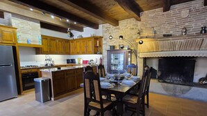 Cozinha com armários de madeira, uma mesa de jantar posta para quatro pessoas e uma lareira de pedra.