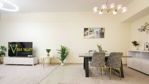 A modern dining area with a table, chairs, a television, and decorative plants. - Silk Valley-Luxury 3B close to Beach (Abu Dhabi)