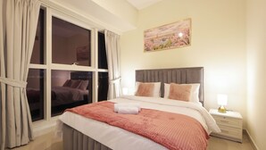 A bedroom with a large bed, a nightstand with a lamp, and a window with curtains. - Silk Valley-Luxury 3B close to Beach (Abu Dhabi)