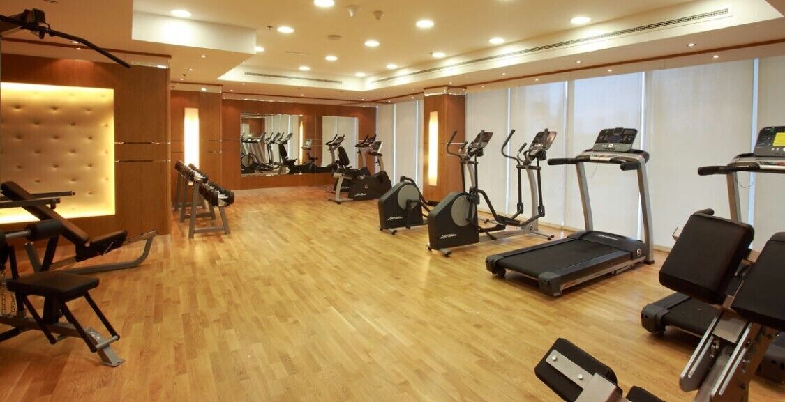 A gym with exercise equipment, wooden flooring, and large windows.