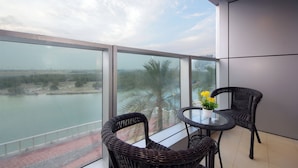 A balcony with wicker chairs and a table, overlooking a body of water and palm trees. - Silk Valley-Luxury 3B close to Beach (Abu Dhabi)