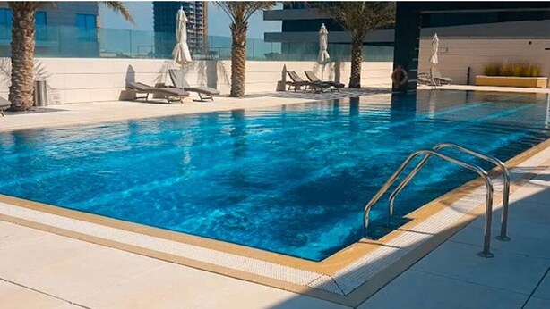 A swimming pool with clear blue water, surrounded by lounge chairs and umbrellas, and palm trees. - Silk Valley-Luxury 3B close to Beach (Abu Dhabi)