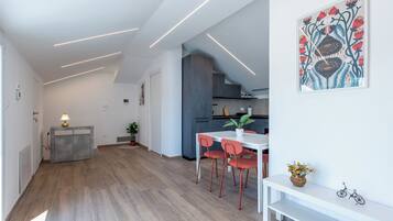 Una cocina moderna con horno empotrado, una zona de comedor con mesa blanca y sillas rojas, y un pasillo con suelo de madera.