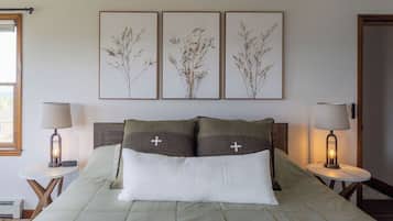A bedroom with a bed, two bedside tables, and three framed botanical prints on the wall.