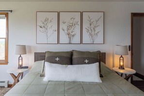 Ett sovrum med en säng, två sängbord och tre inramade botaniska illustrationer på väggen.