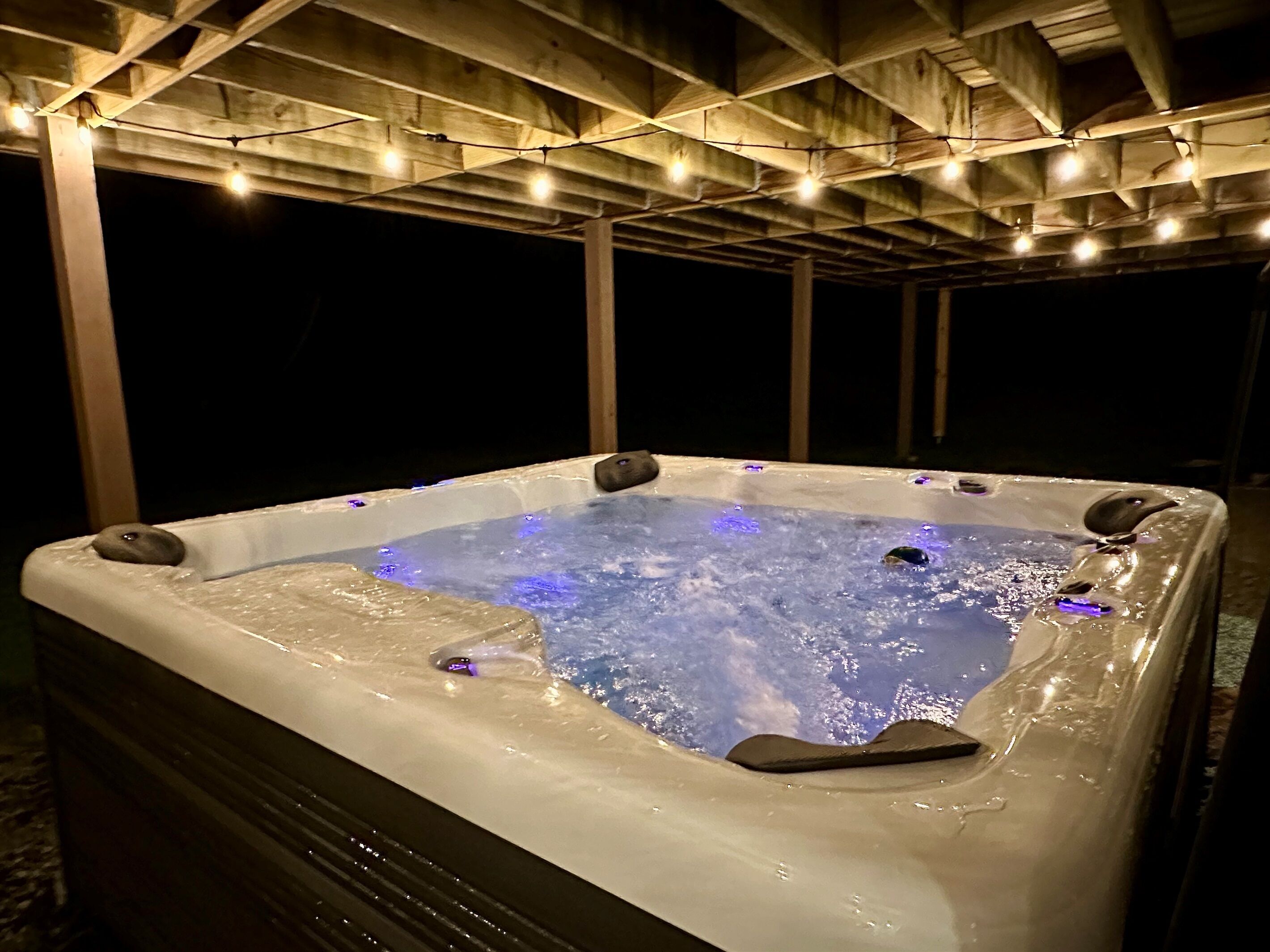 A hot tub under a wooden pergola with string lights.