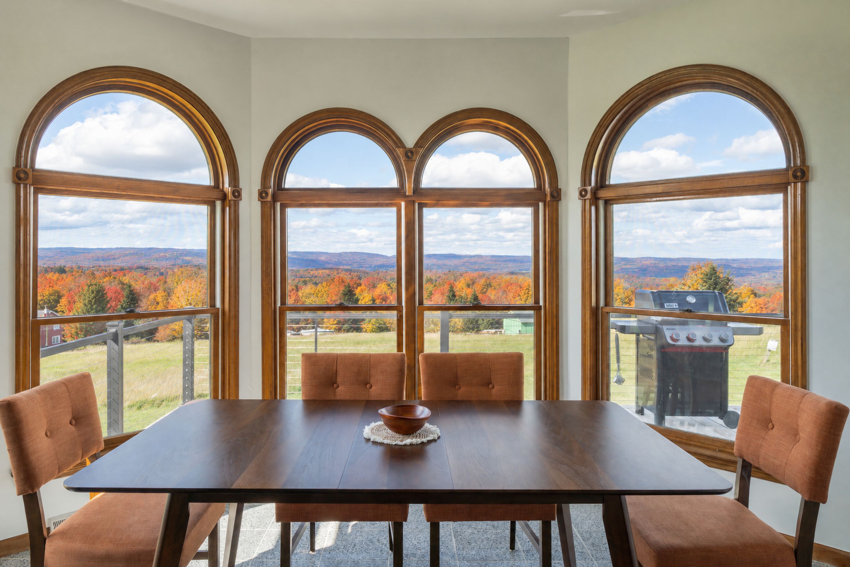 Un espace repas comprenant une table et des chaises, de grandes fenêtres en arc de cercle et une vue sur un paysage montagneux.