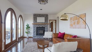 Un salón amplio con chimenea de piedra, sofás de cuero y un ventanal con vistas a una terraza.