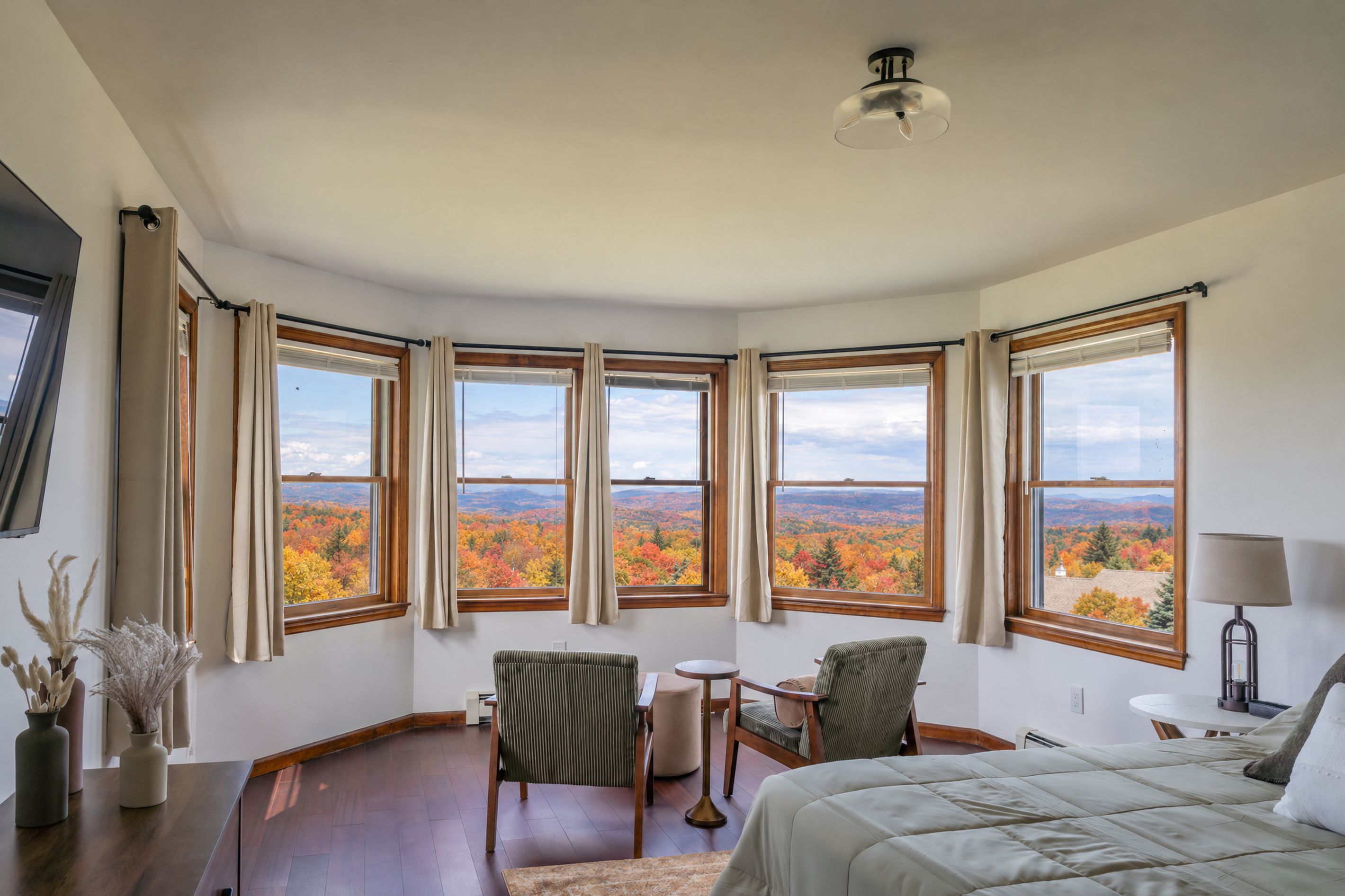 A bedroom with a large window offering a view of autumn foliage.