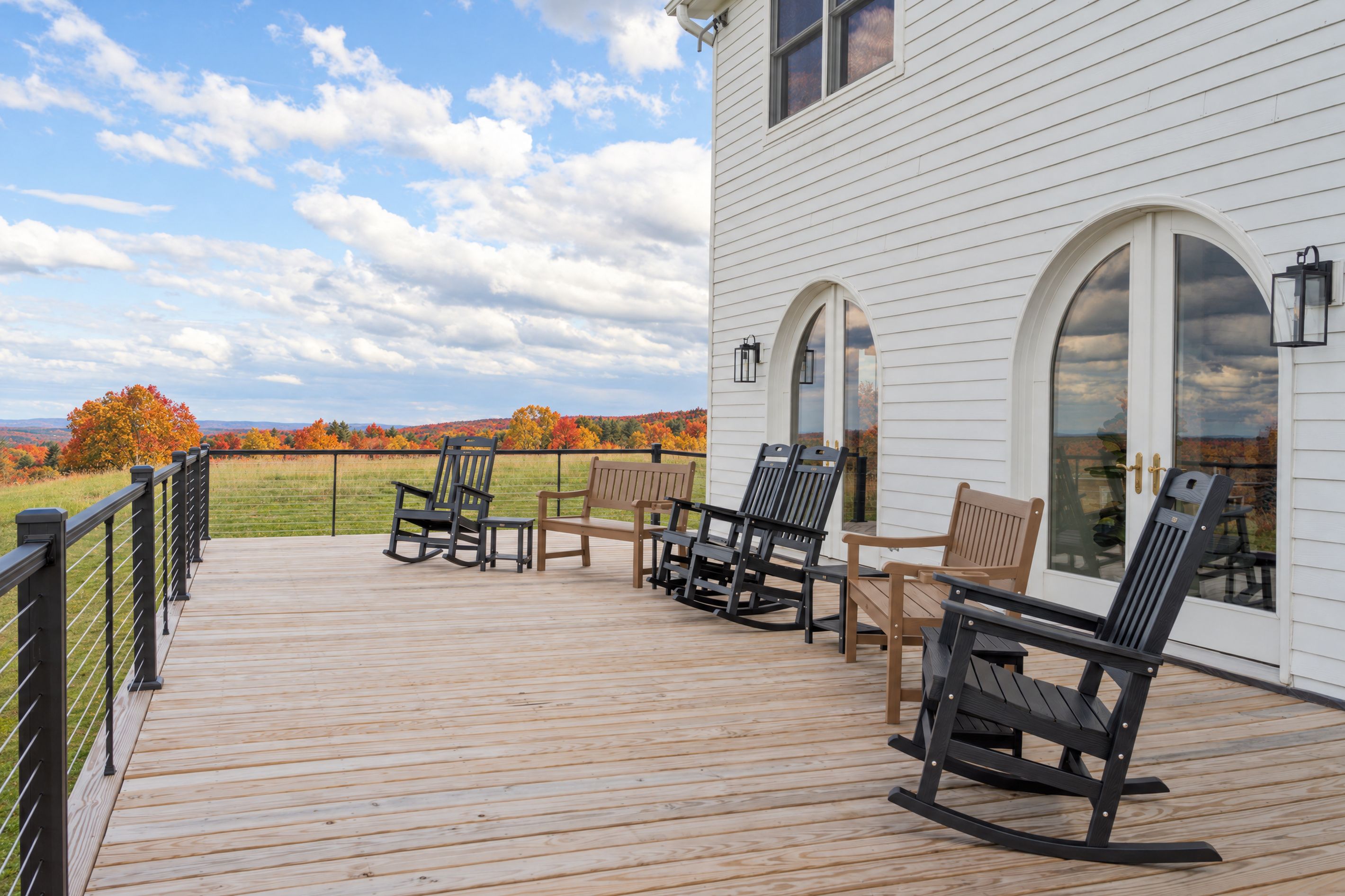 A wooden deck with outdoor furniture, a white building with arched windows, and a view of autumn foliage.