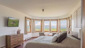 Un dormitorio con una cama grande, un escritorio y vistas al exterior a través de amplios ventanales.