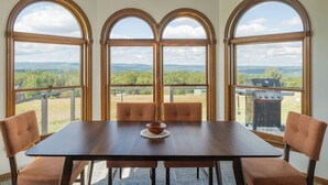 Un comedor con mesa y sillas, ventanas arqueadas amplias y vista al exterior.