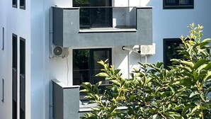 A modern multi-story building with balconies, large windows, and air conditioning units.