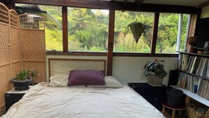 Une chambre à coucher avec un lit, une fenêtre donnant sur un paysage verdoyant, une bibliothèque et une plante en pot.