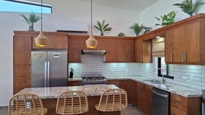 Une cuisine moderne avec des meubles en bois, un réfrigérateur en acier inoxydable, une cuisinière à gaz et trois tabourets de bar en osier.