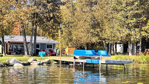 A lakeside property with a dock, a covered seating area, and a house in the background.