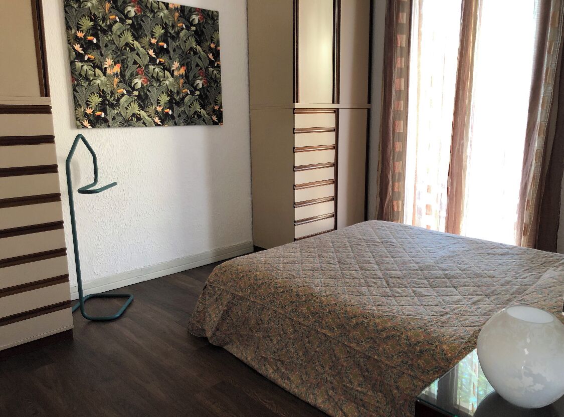 Una camera da letto con un letto, un quadro, un termosifone e una finestra con tende.