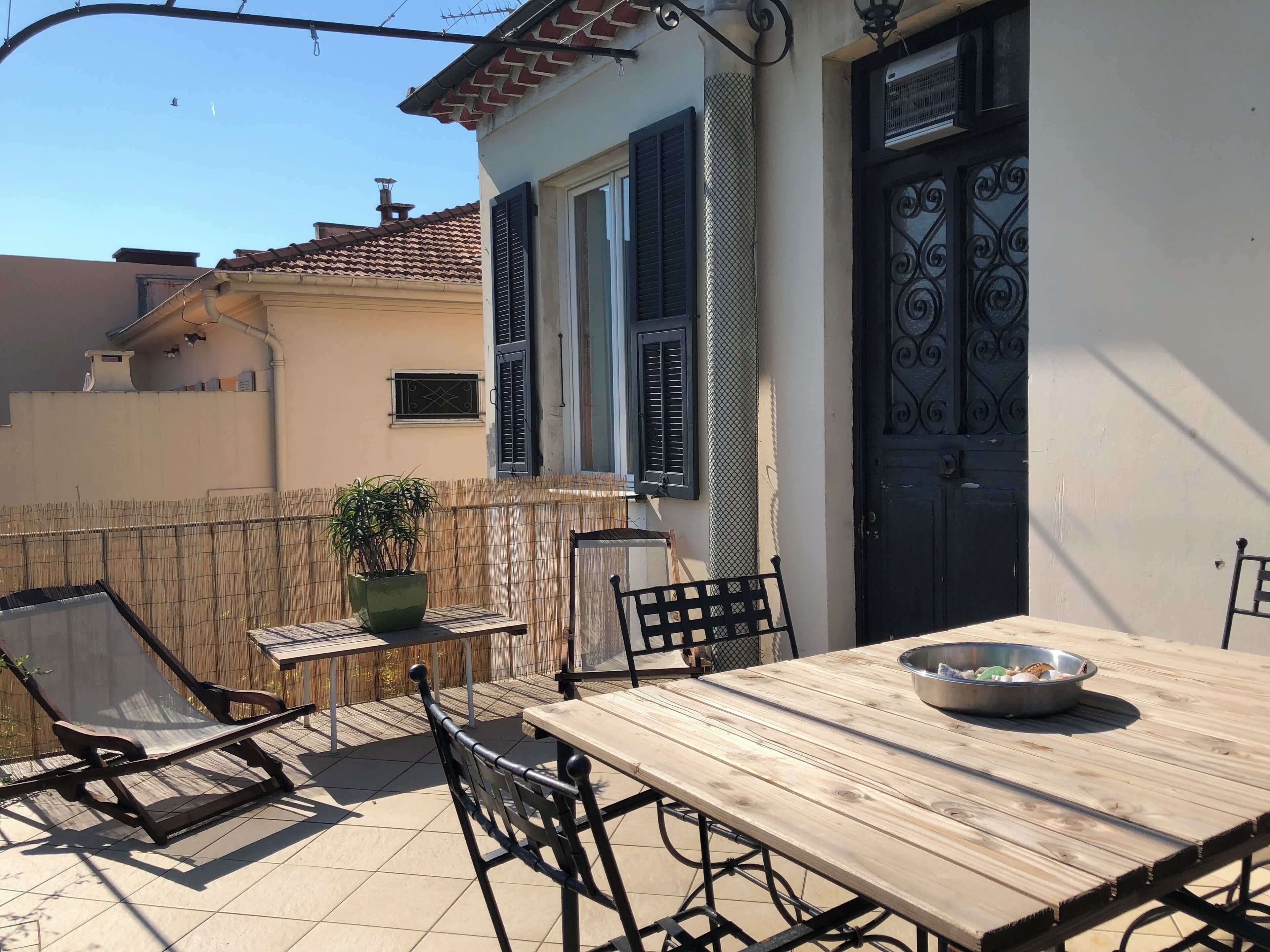 Un patio esterno con tavolo e sedie in legno, una pianta in vaso e una ciotola di metallo sul tavolo.