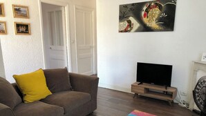 A living room with a brown sofa, a colorful coffee table, a flat-screen TV on a wooden stand, and a painting on the wall.