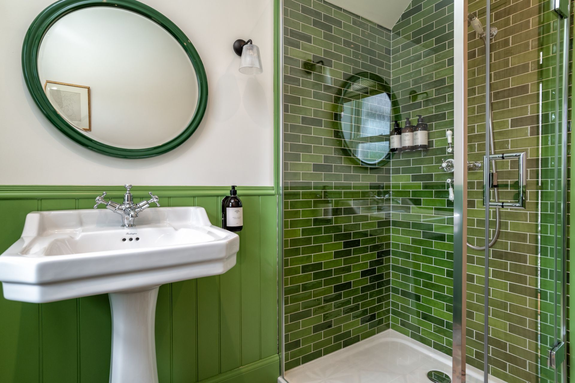 Een badkamer met een groene wastafel, een ronde spiegel en een douche met groen betegelde wanden.