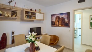 A modern living room with a dining table, chairs, a TV, and decorative items.