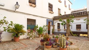 A courtyard with potted plants, a tiled floor, and a building with a tiled roof and balconies.