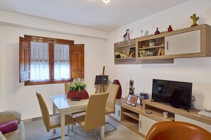 Un espace repas comprenant une table, des chaises, un téléviseur et une étagère où sont disposés des objets décoratifs.