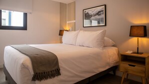 A neatly made bed with a white comforter and a brown throw blanket, a bedside table with a lamp, and a framed picture on the wall. - w Sunlit 1BR w Private Balcony in Miraflores (Lima)