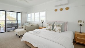 Un dormitorio con una cama grande, ventilador de techo, aire acondicionado, sofá y vistas a través de una puerta corrediza de vidrio.