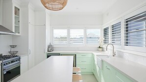Una cocina moderna con armarios blancos, una isla grande, una estufa a gas y una ventana con persianas.