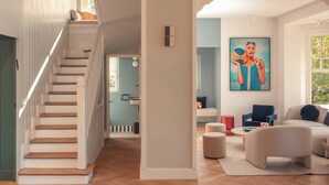 A spacious living area with a wooden staircase, a large painting, and a cozy seating arrangement. - Villa des Rêves: Luxury in Villers, Pool, Jacuzzi & Padel court, A/C, close to Deauville (Villers-sur-Mer)