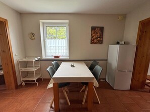 Un coin repas comprenant une table, des chaises, une fenêtre avec vue, un réfrigérateur et une étagère.