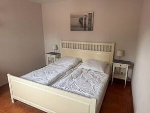 Un llit de matrimoni amb capçalera, dues taules de nit amb làmpades i un quadre penjat a la paret.