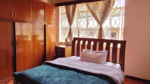 A bedroom with a wooden ceiling, a bed with a blue and white striped bedspread, wooden wardrobe, and a window with curtains. - Tina's ngong hills cottage - country living (Kajiado County)
