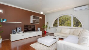 Ein modernes Wohnzimmer mit Flachbildfernseher, weißem Sofa und einem großen Bogenfenster.