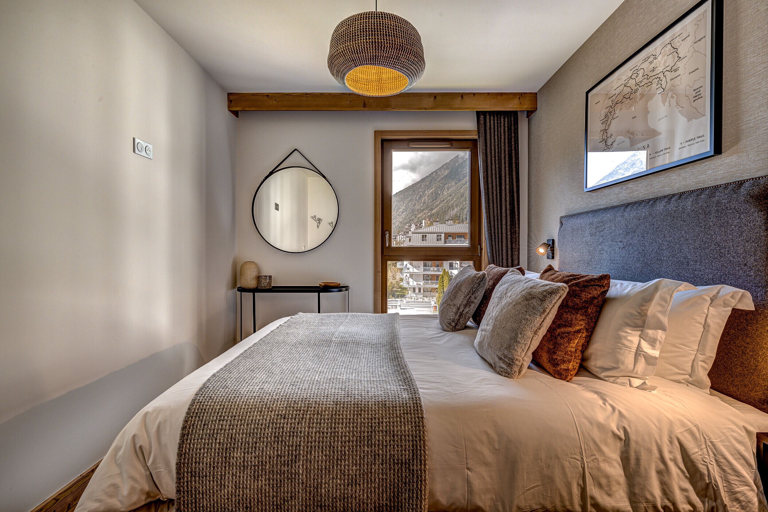 Een slaapkamer met een bed, een spiegel, een kaart aan de muur en een raam met uitzicht op bergen.