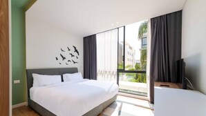 Habitación de hotel moderna con una cama grande, televisión de pantalla plana y balcón con vistas a edificios y zonas verdes.