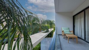 Ein moderner Balkon mit Holztisch und grünem Stuhl, mit Blick auf einen angelegten Garten mit Palmen.