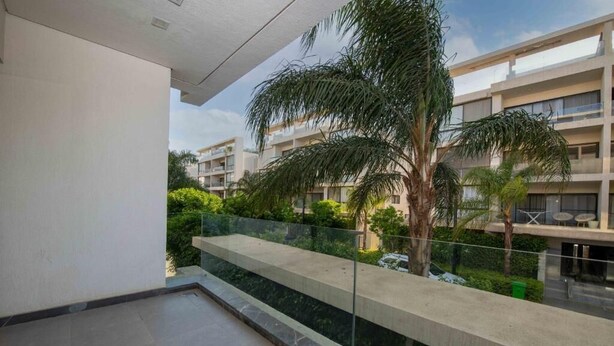 Un apartamento moderno con balcón que da a un jardín exuberante y edificios vecinos.