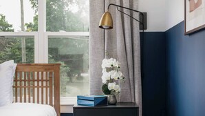 A bedroom with a wooden headboard, a bedside table with a blue box, a vase with white flowers, and a window with curtains. - Modern 4BR Retreat for 12, Near Downtown Nash! (Nashville)