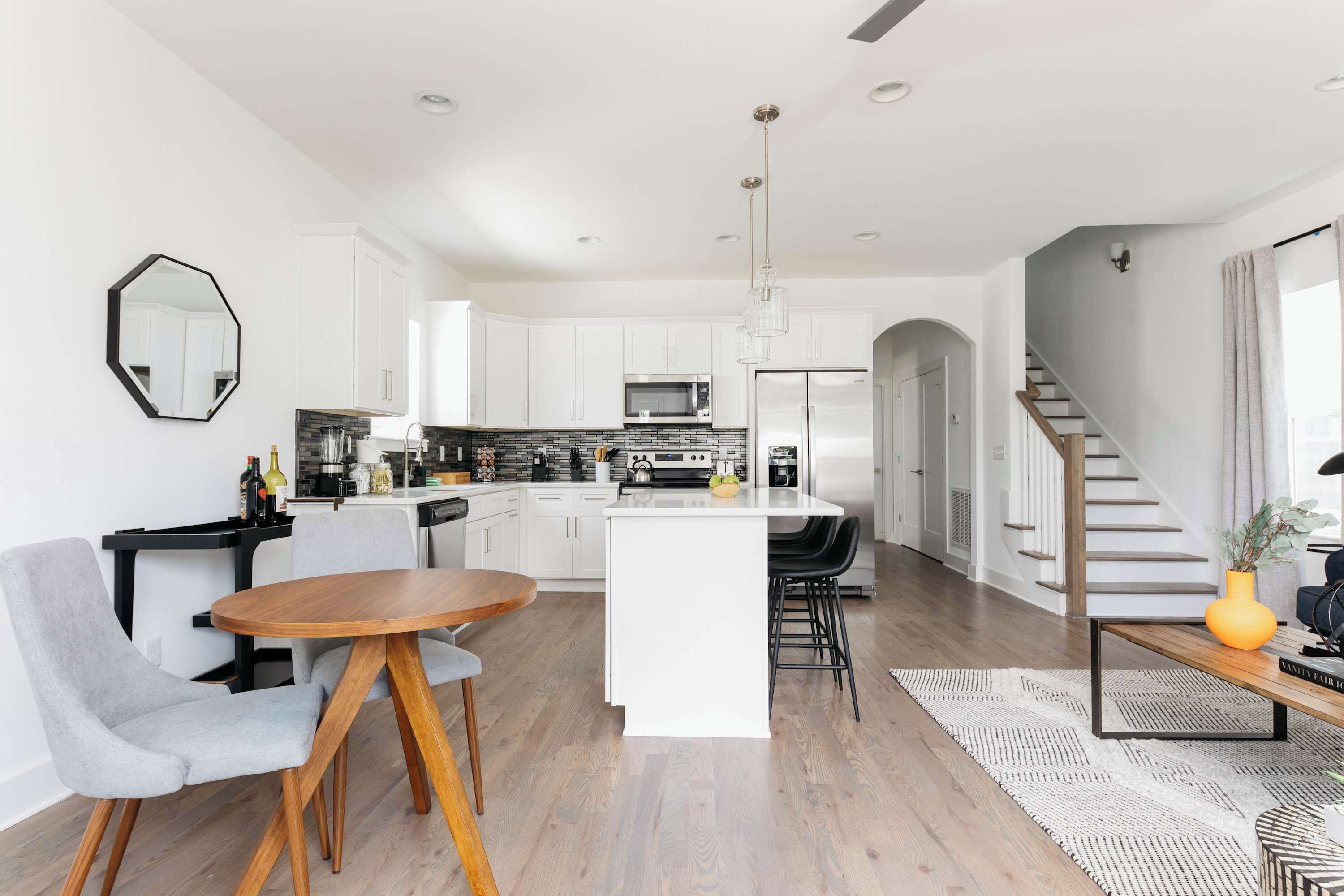 A modern kitchen with white cabinetry, a central island, and a dining area with a round wooden table and grey chairs.