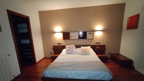 A bedroom with a large bed, two bedside tables, a nightstand, a mirror, and wall-mounted lights. - DALT DES PADRÓ (Muro)