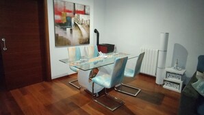 A dining area with a glass table and chairs, a painting on the wall, and a radiator. - DALT DES PADRÓ (Muro)